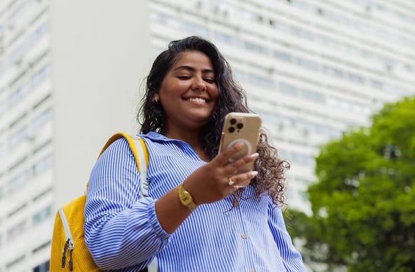 Estudante sorrindo enquanto usa o celular na rua